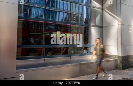 Londres, Royaume-Uni: Une personne marchant le long de Bishopsgate dans la City de Londres avec le flou de mouvement. Un bus rouge londonien se reflète dans la fenêtre du bâtiment. Banque D'Images