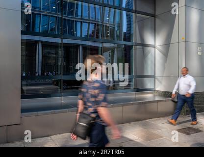 Londres, Royaume-Uni: Deux personnes marchant le long de Bishopsgate dans la City de Londres avec le flou de mouvement. La scène de la rue se reflète dans la fenêtre du bâtiment. Banque D'Images