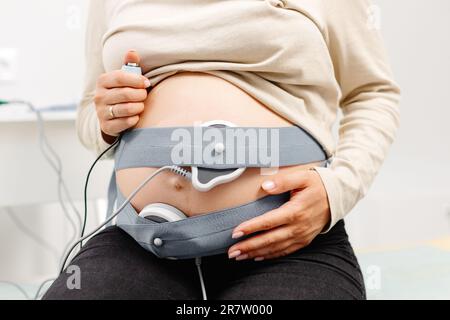 Femme enceinte vérifiant le rythme cardiaque fœtal par surveillance fœtale. Mère enceinte avec sage-femme qui ajuste les capteurs hors cardiotocographie (CTG). Banque D'Images