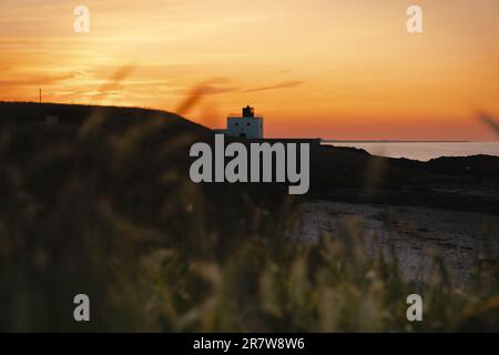 Le phare de Bamburgh avec son visage souriant au coucher du soleil avec Lindisfarne en arrière-plan Banque D'Images