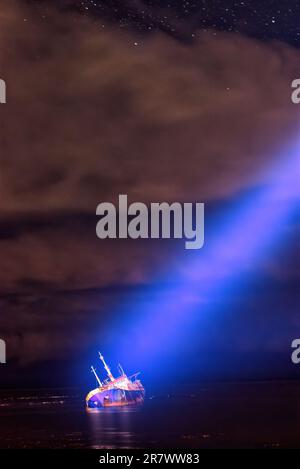 Un faisceau lumineux et concentré de lumière est dirigé depuis le ciel vers un navire qui s'est échoué et qui s'affiche sur son côté Banque D'Images