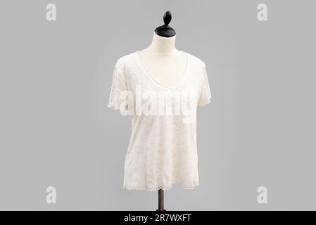 Le haut à manches courtes à motif floral blanc est suspendu sur un mannequin sans tête blanc. isolé par un fond gris sonore Banque D'Images