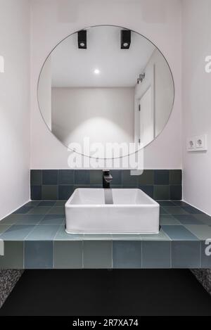 salle de bains moderne avec carrelage vert lavabos en porcelaine miroir circulaire boiseries blanches accents noirs et sol en terrazzo gris Banque D'Images