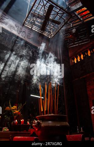 La lumière du soleil se diffuse dans un évent mettant en lumière la fumée des bougies d'encens qui brûlent à l'intérieur d'un temple bouddhiste antique. Vietnam Banque D'Images