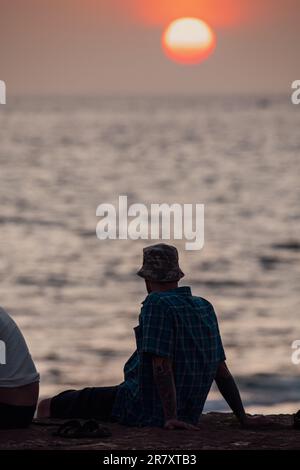 Galle, Sri Lanka - 02 03 2022: Un touriste avec un chapeau est assis et bénéficie de la vue sur le coucher du soleil. Banque D'Images