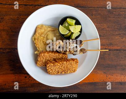 Tempe et Sate Ayam, tempeh et satay de poulet, avec des lamelles de kaffir sur une assiette blanche Banque D'Images