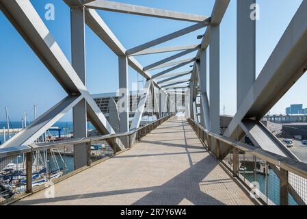 Un pont de treillis industriel, esthétiquement piétonnier, mène au-dessus du forum du port de plaisance de Barcelone. L'immense panneau solaire est un point de repère dans le port Banque D'Images