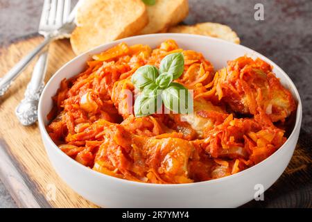 Morceaux de poisson de mer blanc compotés de légumes dans une sauce tomate servis avec du pain grillé sur une planche en bois sur la table. horizontale Banque D'Images