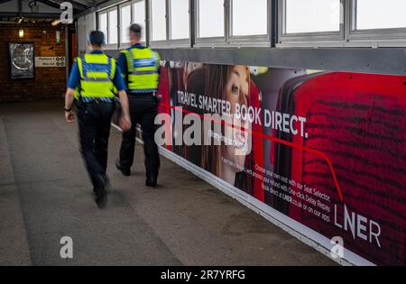 Des policiers de la police des transports britannique passent devant une palissade publicitaire pour le London North Eastern Railway (LNER) pour des voyages plus intelligents et pour réserver directement Banque D'Images