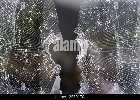 Gros plan d'une fenêtre en verre cassée. Il y a un grand trou irrégulier au centre, avec des fissures rayonnant. Banque D'Images