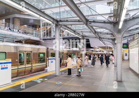 Les navetteurs japonais attendent sur les lignes de plateforme désignées pour le prochain train express, tandis que le train local est sur le point de partir à la gare d'Osaka. Banque D'Images