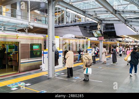 Les navetteurs japonais attendent sur les lignes de plate-forme désignées pour le prochain train express, tandis que certaines personnes s'embarquent encore dans le train local. Osaka. Banque D'Images