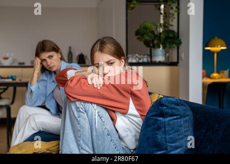 Frustré offensé, une adolescente s'étreint à genoux et regarde loin. Maman est assise à côté Banque D'Images