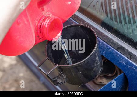 Verser le carburant dans un réservoir de carburant de voiture à l'aide d'un entonnoir à partir d'une bouteille rouge Banque D'Images