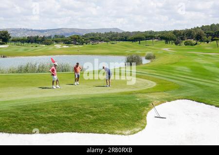 Golfeurs sur le vert 18th avec le danger de l'eau et 18th fairway derrière, Laranjal golf course, Algarve, Portugal. Banque D'Images