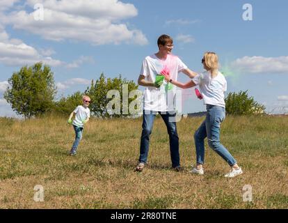 La famille caucasienne joue avec le colorant coloré à la fête d'anniversaire ou célèbre le Holi Color Festival, en lançant la poudre multicolore. Joyeux parent, enfants joue Banque D'Images