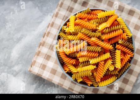 Pâtes fusilli crues sur béton. Pâtes rotini ou fusilli de trois couleurs sur une serviette en lin. Cuisine italienne Banque D'Images