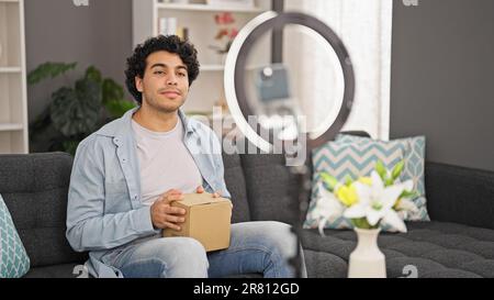 Jeune homme latin tenant une boîte en carton enregistrer vidéo tutoriel à la maison Banque D'Images