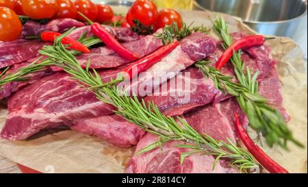 Rouleau de papier d'aluminium avec morceau de viande crue, tomates, romarin et épices sur table en bois de couleur, gros plan Banque D'Images