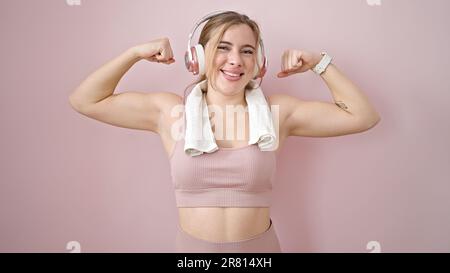 Jeune femme blonde écoutant de la musique faisant un geste fort avec les bras sur fond rose isolé Banque D'Images