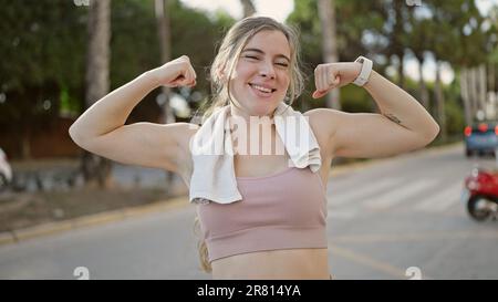 Jeune femme blonde portant des vêtements de sport faisant un geste fort avec les bras dans la rue Banque D'Images