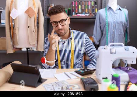 Homme hispanique avec couturier de la barbe designer travaillant à l'atelier pointant vers l'oeil vous regardant le geste, expression suspecte Banque D'Images