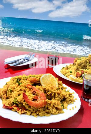 Paella par la côte de mer en Espagne. Vacances typiques côte populaire rustique espagnol repas de fruits de mer cuit et préparé au bord de la mer, dans la cafétéria locale bar restaurant avec vue spectaculaire, servi traditionnellement avec vin rouge local frais Espagne Banque D'Images