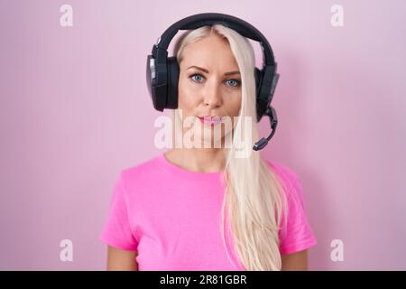 Femme caucasienne écoutant de la musique en utilisant des écouteurs détendu avec une expression sérieuse sur le visage. simple et naturel à regarder l'appareil photo. Banque D'Images