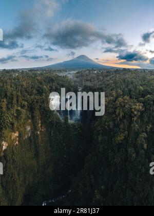 Vue d'en haut, vue aérienne stupéfiante des chutes d'eau de Tumpak Sewu également connu sous le nom de Coban Sewu avec le volcan Semeru au loin, la Régence de Malang Banque D'Images