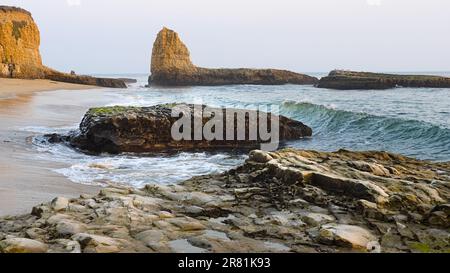 Vagues arrivant à la plage avec des rochers et des falaises. Banque D'Images