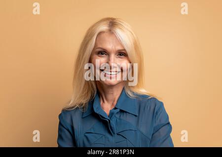 Portrait d'une belle femme blonde senior posant sur le beige Banque D'Images