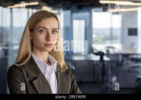 Portrait d'une jeune femme d'affaires sérieuse et confiante avocat. Elle se tient dans le centre de bureau dans un costume d'affaires, croise ses bras sur sa poitrine, regarde la caméra. Banque D'Images