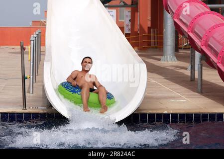 Un homme heureux dans un cercle gonflable descend sur un toboggan aquatique dans un parc aquatique. Promenade sur le tube d'eau, profiter des vacances d'été, station balnéaire Banque D'Images