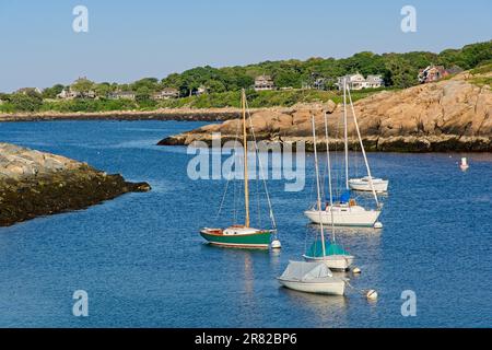 Les voiliers amarrés dans le canal du port de Rockport délimité par la culture de roche et la jetée en pierre avec des maisons éloignées bordant le rivage Banque D'Images