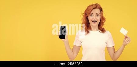 Femme isolée visage portrait, bannière avec maquette copie espace. Jeune femme excitée isolé sur fond jaune à l'aide de téléphone portable tenant la carte de crédit Banque D'Images