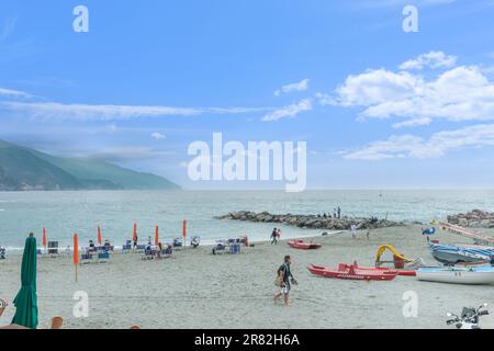 Monterosso - Italie 24 avril 2011; couple marchant hors de la plage avec d'autres se détendant sur la plage méditerranéenne avec des bateaux. Banque D'Images