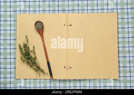 Livre de recettes vierge et thym sur nappe à carreaux, vue de dessus. Espace pour le texte Banque D'Images