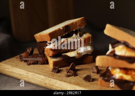 Délicieux sandwiches guimauves avec du pain et du chocolat sur une planche en bois, en gros plan Banque D'Images