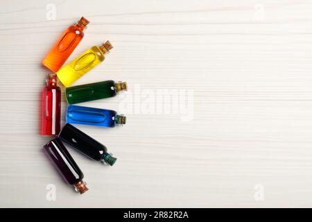 Bouteilles en verre avec différentes couleurs alimentaires sur table en bois blanc, plat. Espace pour le texte Banque D'Images