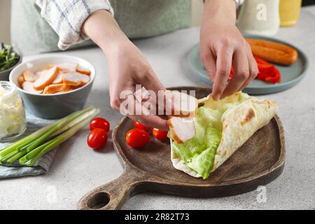 Femme cuisant de délicieux enveloppement de pita avec du poulet et de la laitue à la table gris clair, gros plan Banque D'Images