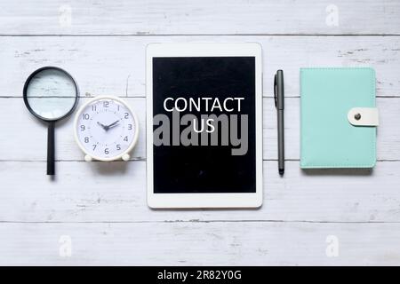 Vue de dessus de la loupe, horloge de table, stylo, ordinateur portable et tablette écrit avec « CONTACTEZ-nous » sur fond blanc en bois. Banque D'Images