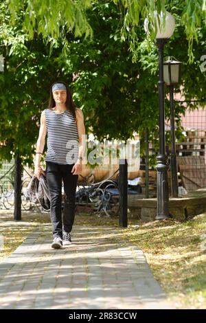 Un jeune homme avec de longs cheveux dans le débardeur et des jeans marche le long du trottoir Banque D'Images