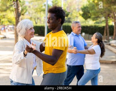 Couples séniors multiraciaux dansant en couple à l'extérieur pendant la journée ensoleillée au parc Banque D'Images