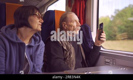 Un couple âgé voyage en train, un senior regarde par la fenêtre et tourne sur un téléphone portable Banque D'Images