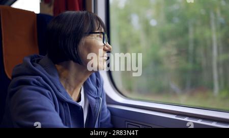 Une femme âgée en lunettes voyage en train et regarde par la fenêtre Banque D'Images