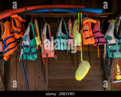Les gilets de sauvetage multicolores sont suspendus sur un mur en bois pour les clients du complexe qui souhaitent pratiquer des activités nautiques, du kayak, du paddleboard, etc Banque D'Images