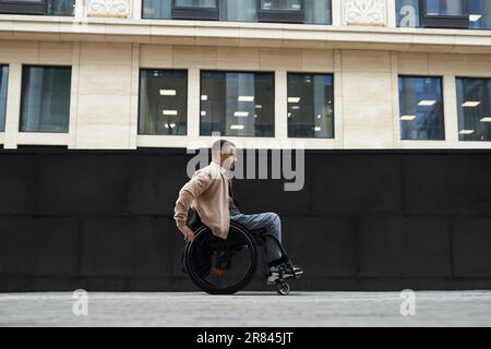 Vue latérale d'un jeune homme en fauteuil roulant le long des rues de la ville Banque D'Images