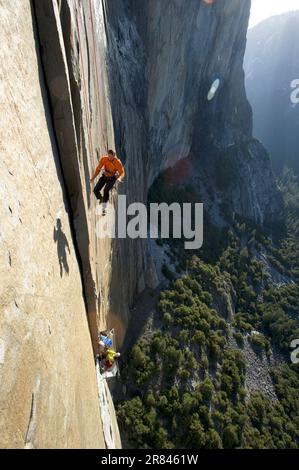 Un homme qui fait une pause dans les terrains d'exécution tandis qu'une femme fait le ventre d'un bord de mer en contrebas sur El Cap dans le parc national de Yosemite, en Californie. Banque D'Images