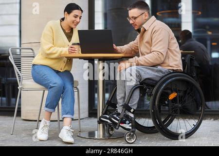 Jeune homme handicapé ayant une réunion d'affaires avec une femme, ils s'asseyant dans un café extérieur et discutant de la présentation en ligne sur ordinateur portable Banque D'Images