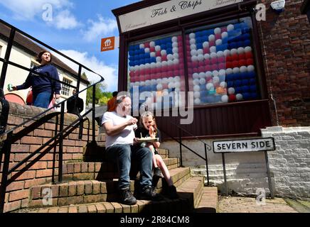 Homme et enfant mangeant du fish and chips à l'extérieur de la boutique de chips décorée pour le couronnement du roi Charles III. Photo de DAVID BAGNALL Banque D'Images